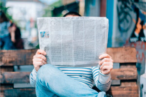 Person sitzt auf einer Parkbank und liest in der Zeitung